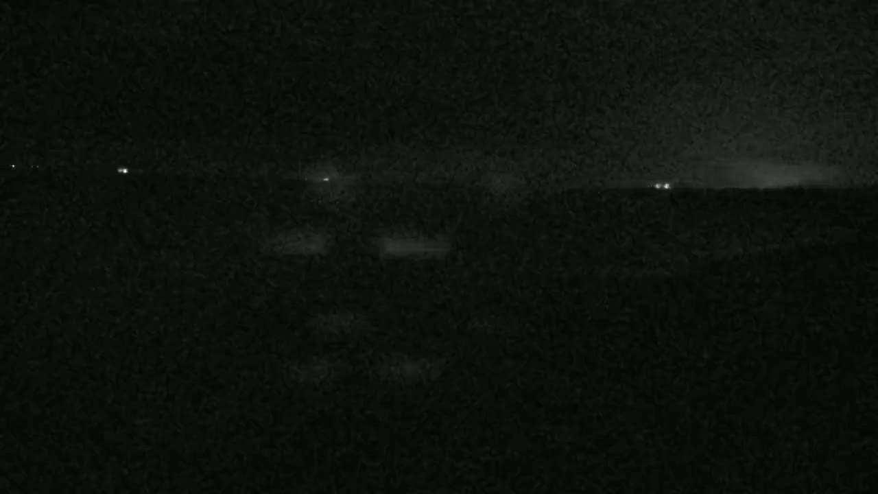 A dark, nighttime landscape is visible, with a few distant lights faintly illuminating the horizon under a cloudy sky.