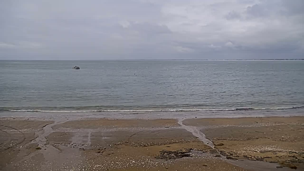A sandy beach stretches to a calm sea under an overcast sky, with a small boat visible in the distance.