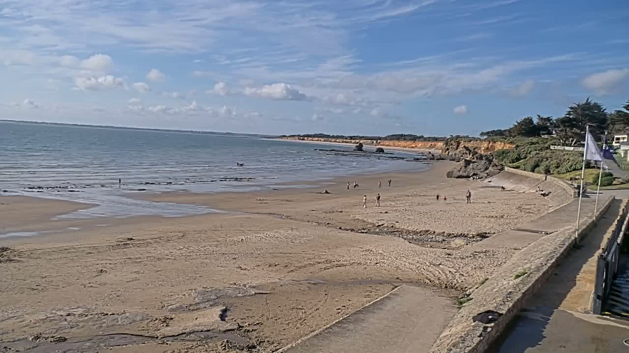 A sandy beach with a few people on it stretches along a calm ocean under a mostly sunny sky.