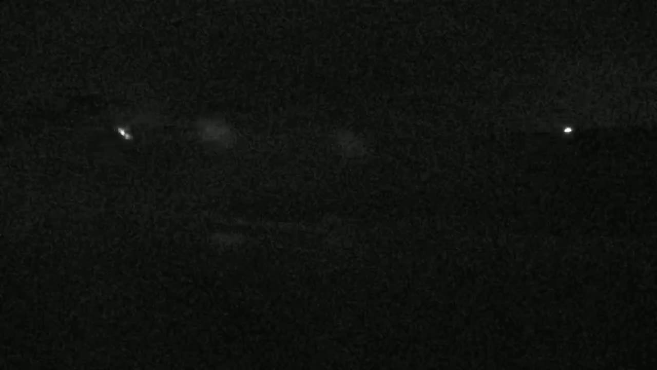 A nighttime, dark image shows a few faint white lights in the distance against a textured, dark background.