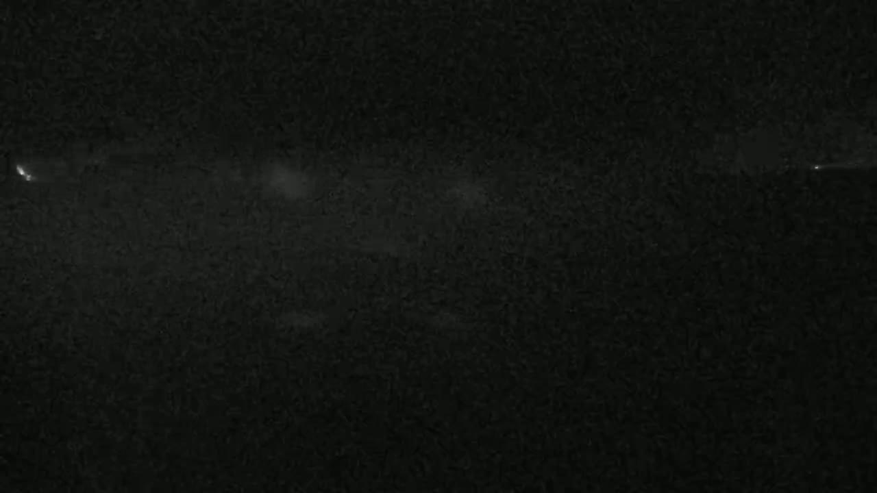 A dark, possibly nighttime, scene shows a faint, horizontal streak of light across a textured, dark surface.