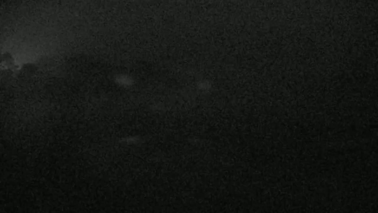A dark, grainy image shows a nighttime outdoor scene with a few indistinct shapes and faint light sources.