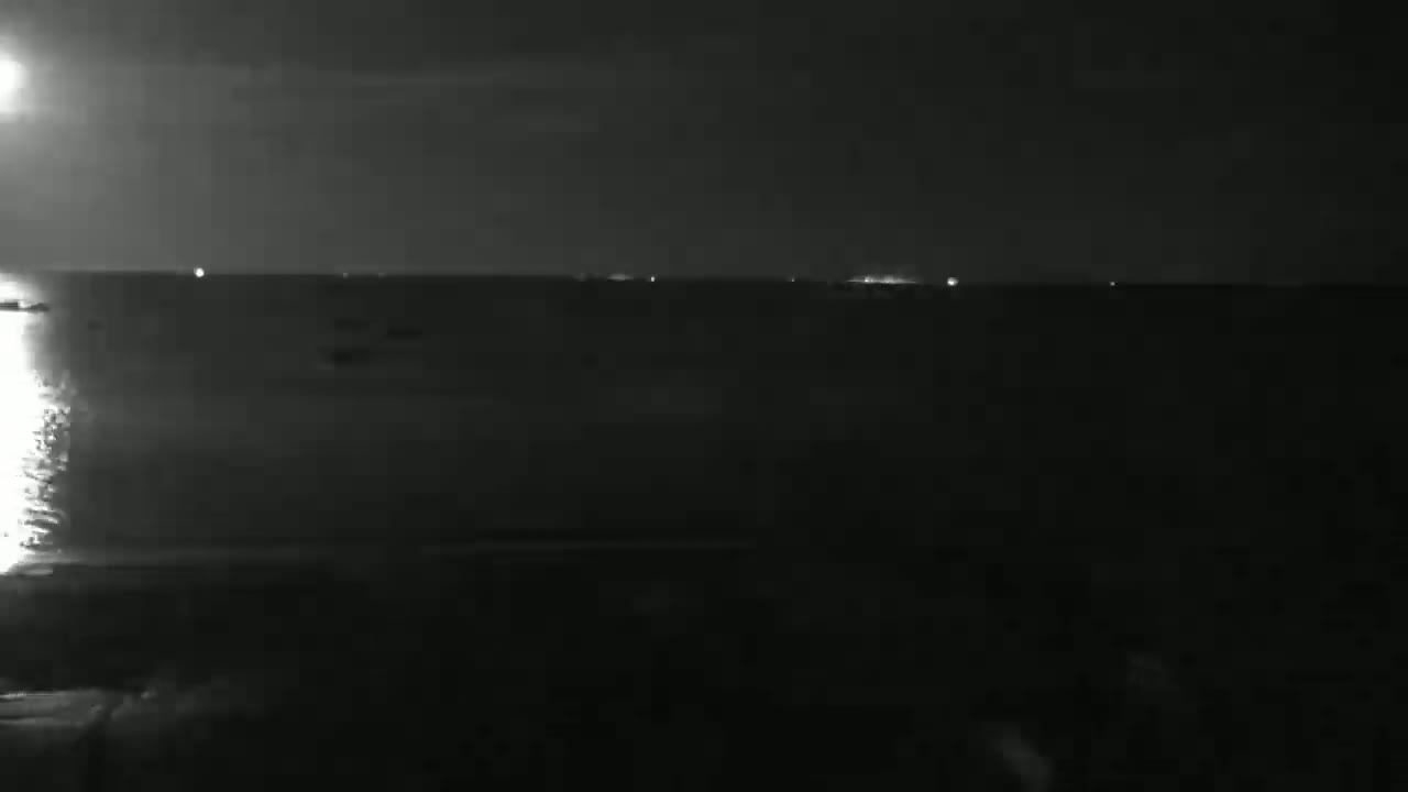 A dark, nighttime view of a body of water with faint lights visible on the horizon.