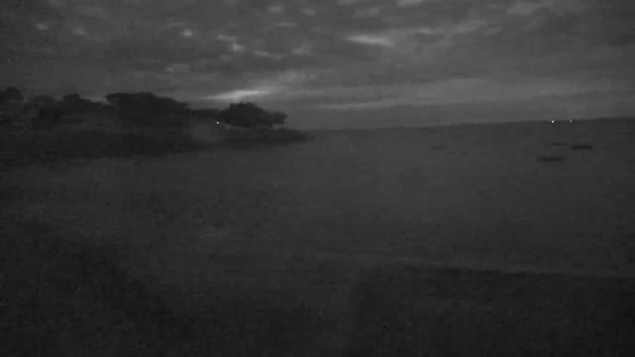 A dark, overcast sky hangs over a calm body of water with a treeline visible in the distance.