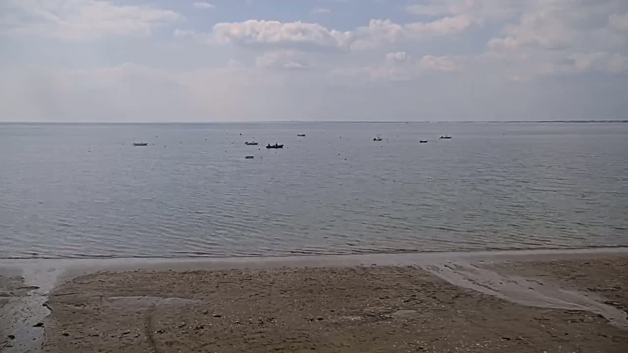 A sandy beach slopes gently down to a calm, grey-blue sea where several small boats are scattered.