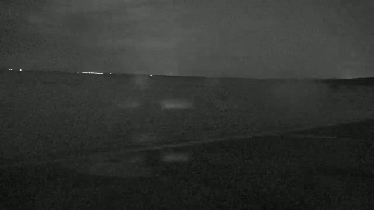 A dark, nighttime landscape shows a body of water under a cloudy sky.