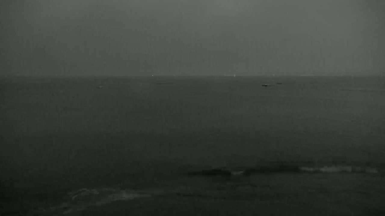 A dark, overcast sky hangs over a calm body of water, with a few distant objects barely visible on the horizon.