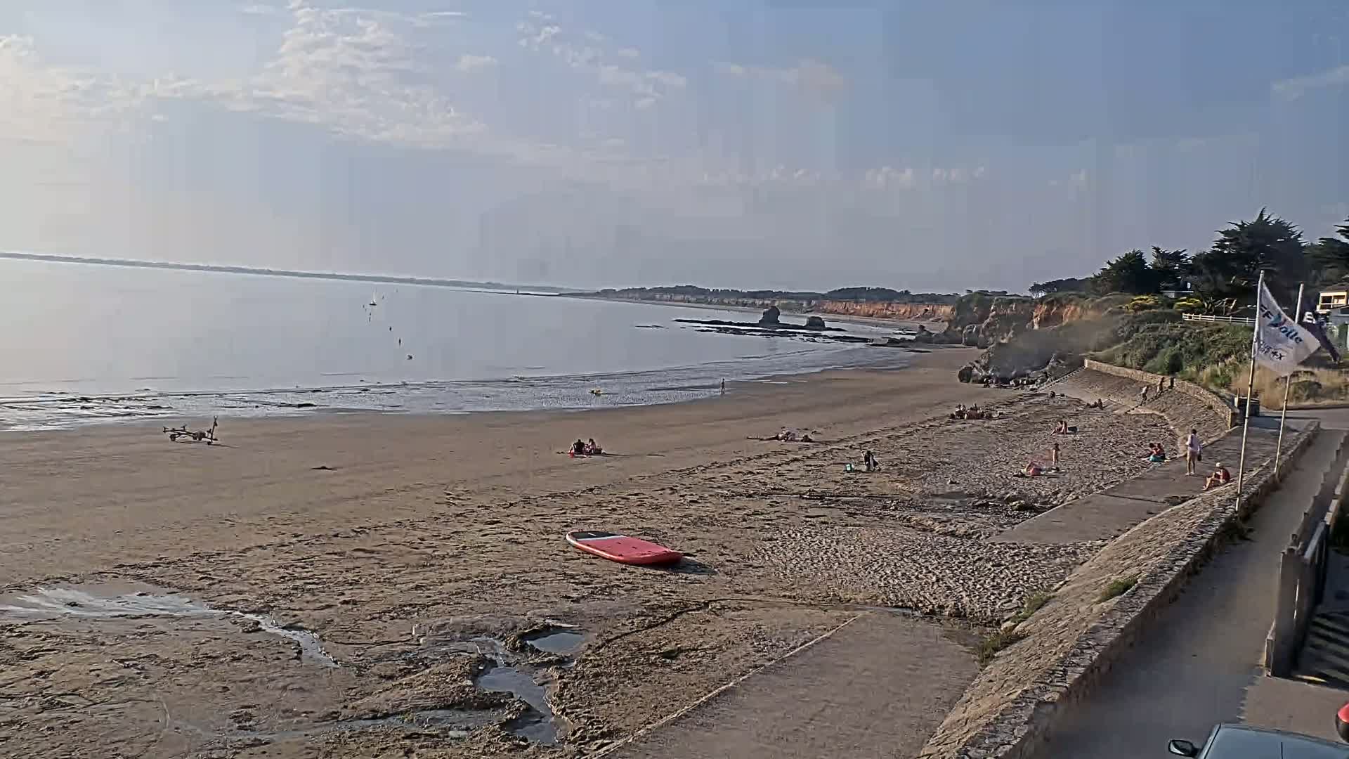 A sandy beach with a few people sunbathing and a calm sea under a partly cloudy sky.