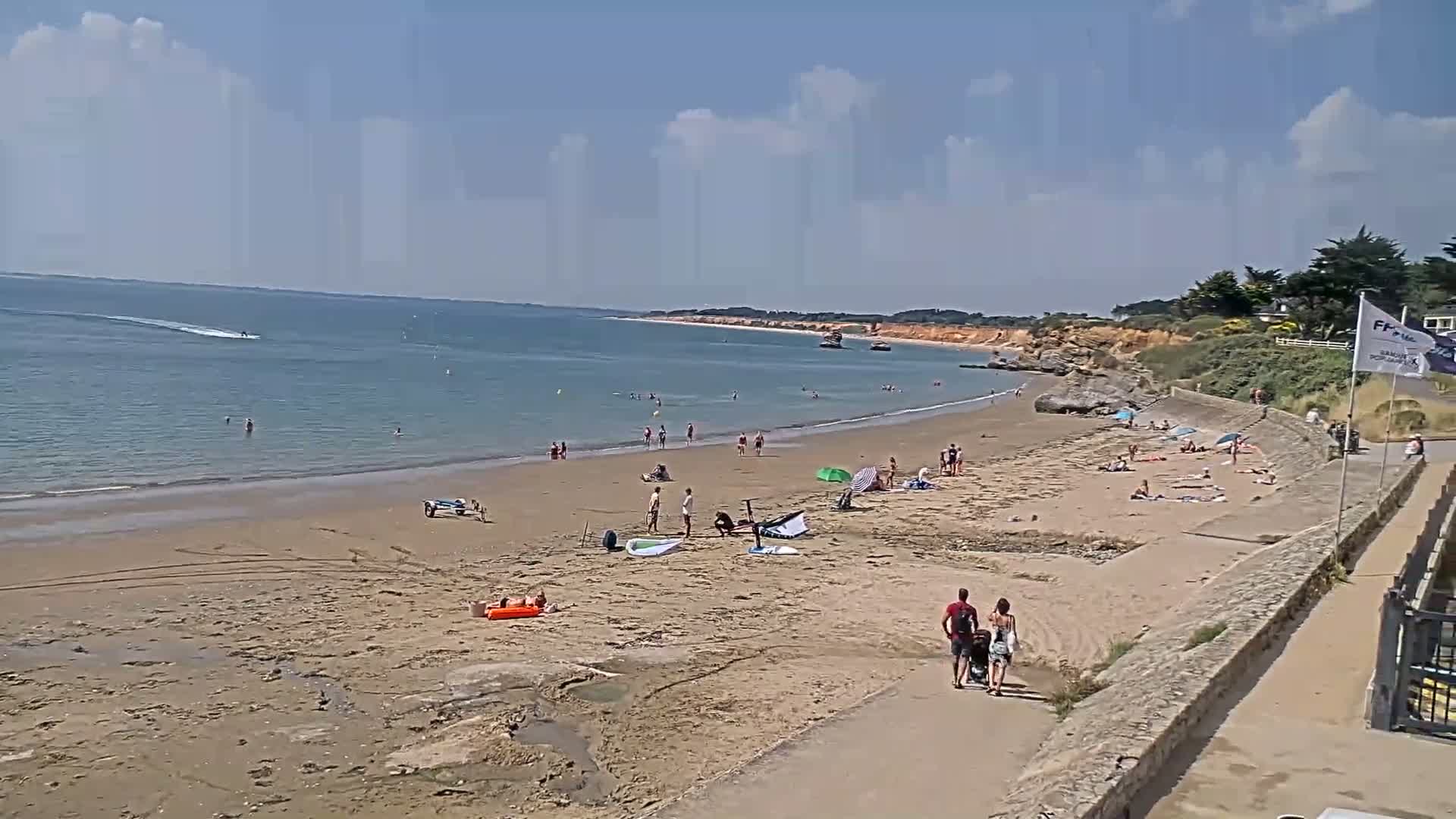 A sandy beach with scattered sunbathers and a calm ocean under a partly cloudy sky.