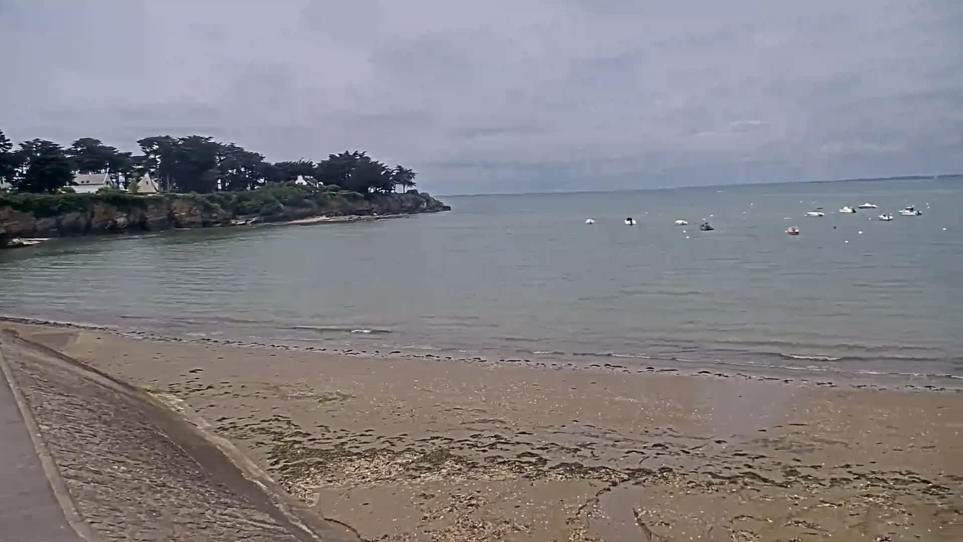 A sandy beach and calm, gray water with several small boats are visible under an overcast sky.