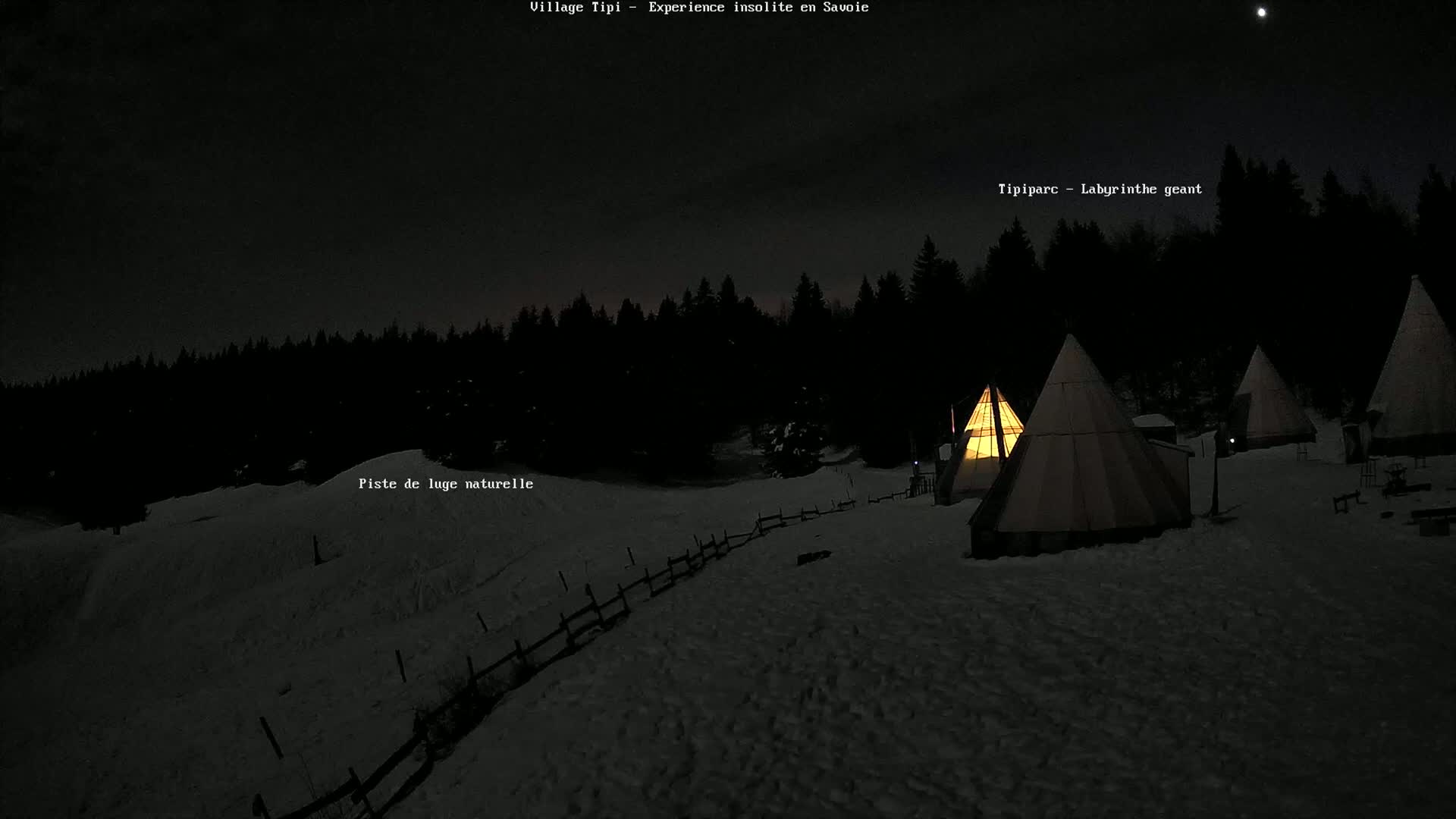 Several illuminated teepees are nestled in a snow-covered landscape under a night sky.