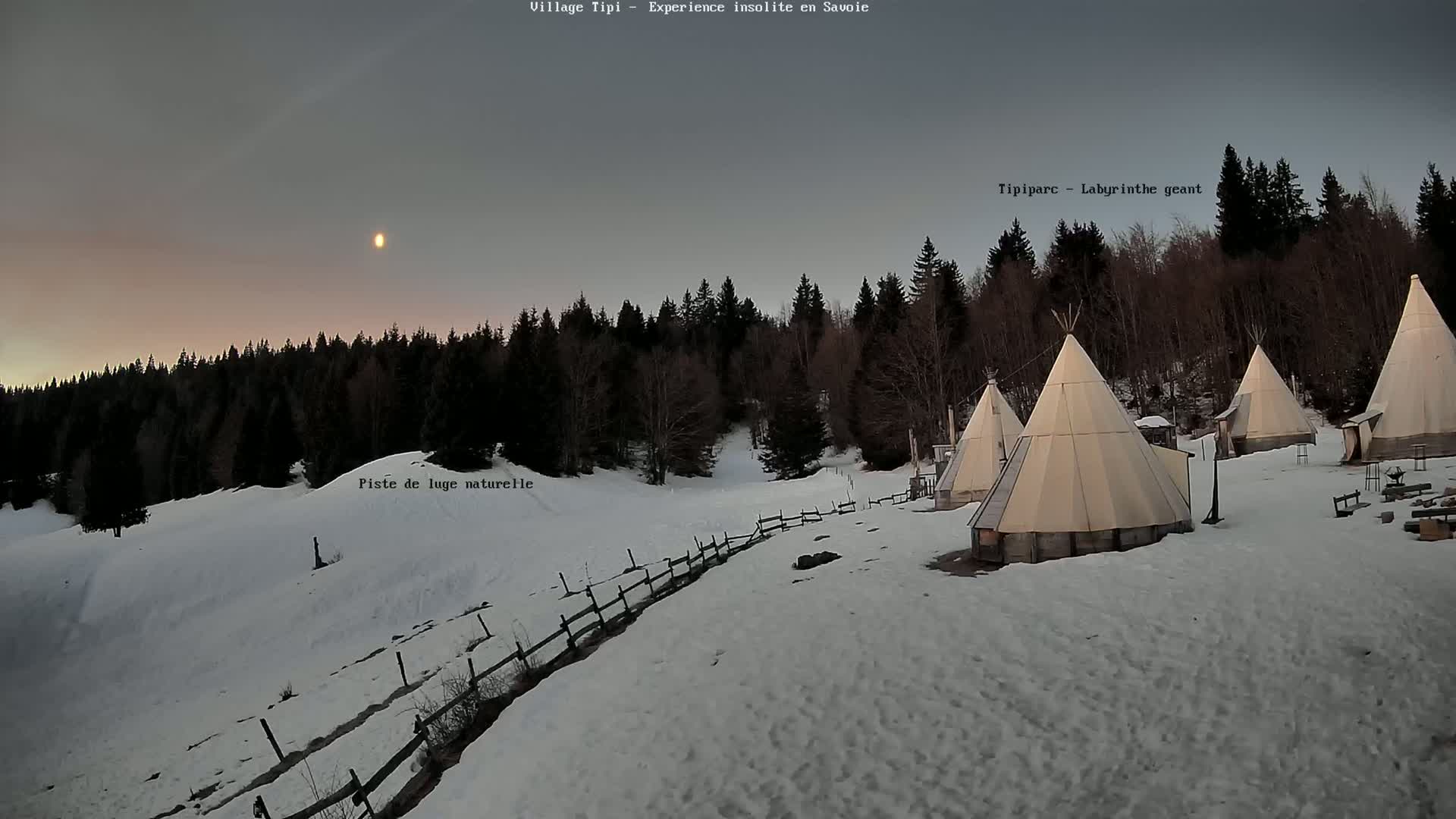 Several teepees are situated on a snow-covered landscape in front of a dark forest, under a twilight sky with a visible moon.