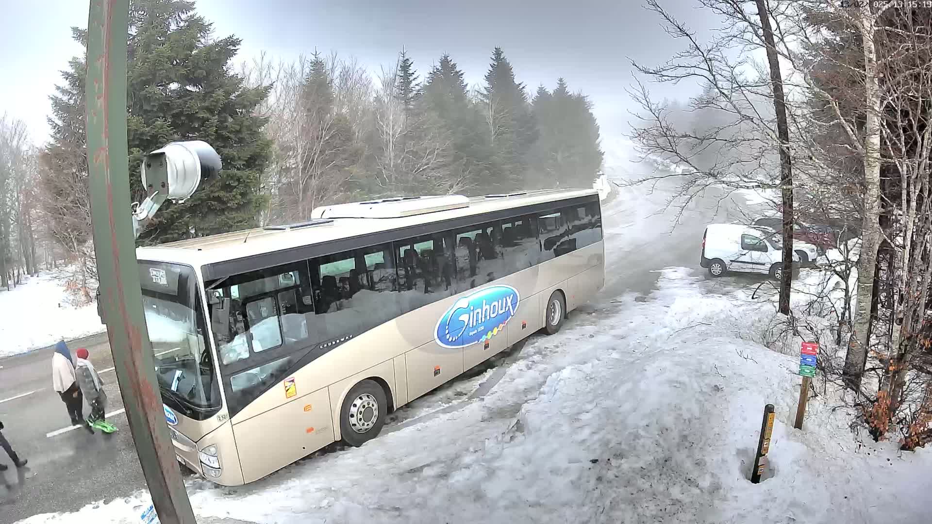 A large beige bus is parked in a snowy area next to a road, with a few other vehicles visible in the background, under foggy conditions.