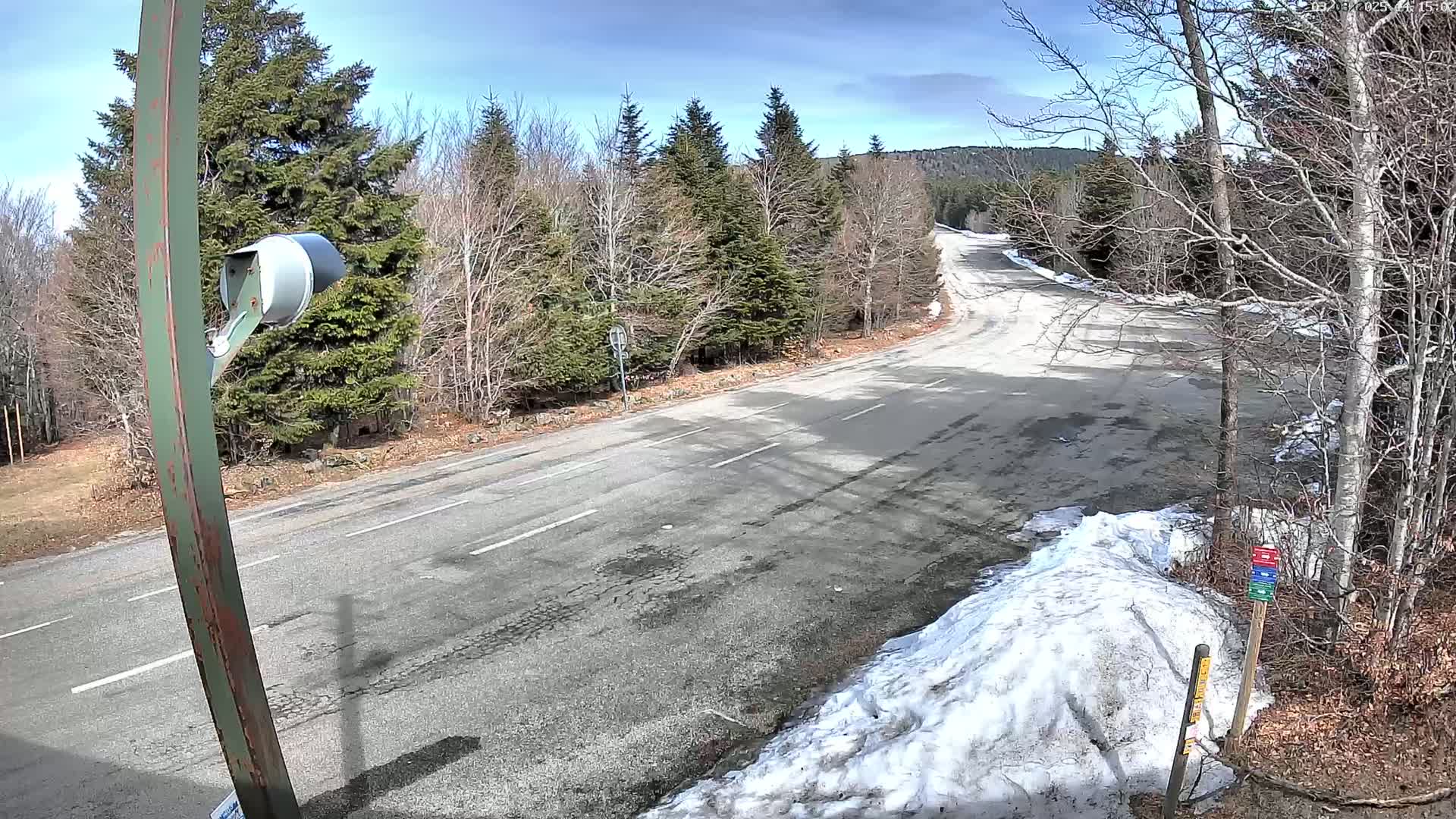 A paved road curves through a mostly barren winter landscape with some remaining snow, under a partly sunny sky.