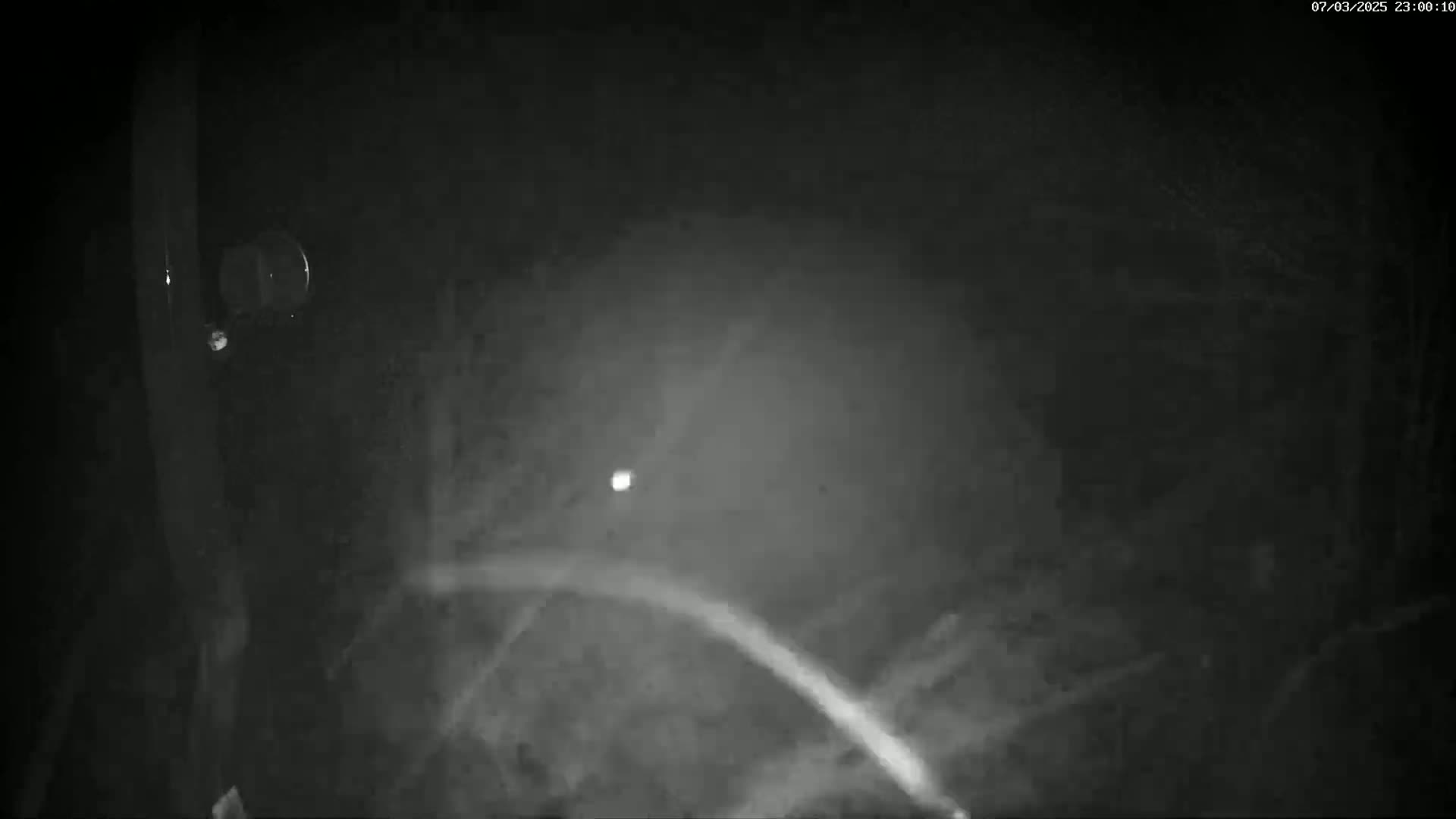 A blurry, nighttime, low-light image shows a small, bright light in the distance and what appears to be a blurry arc of light in the foreground.