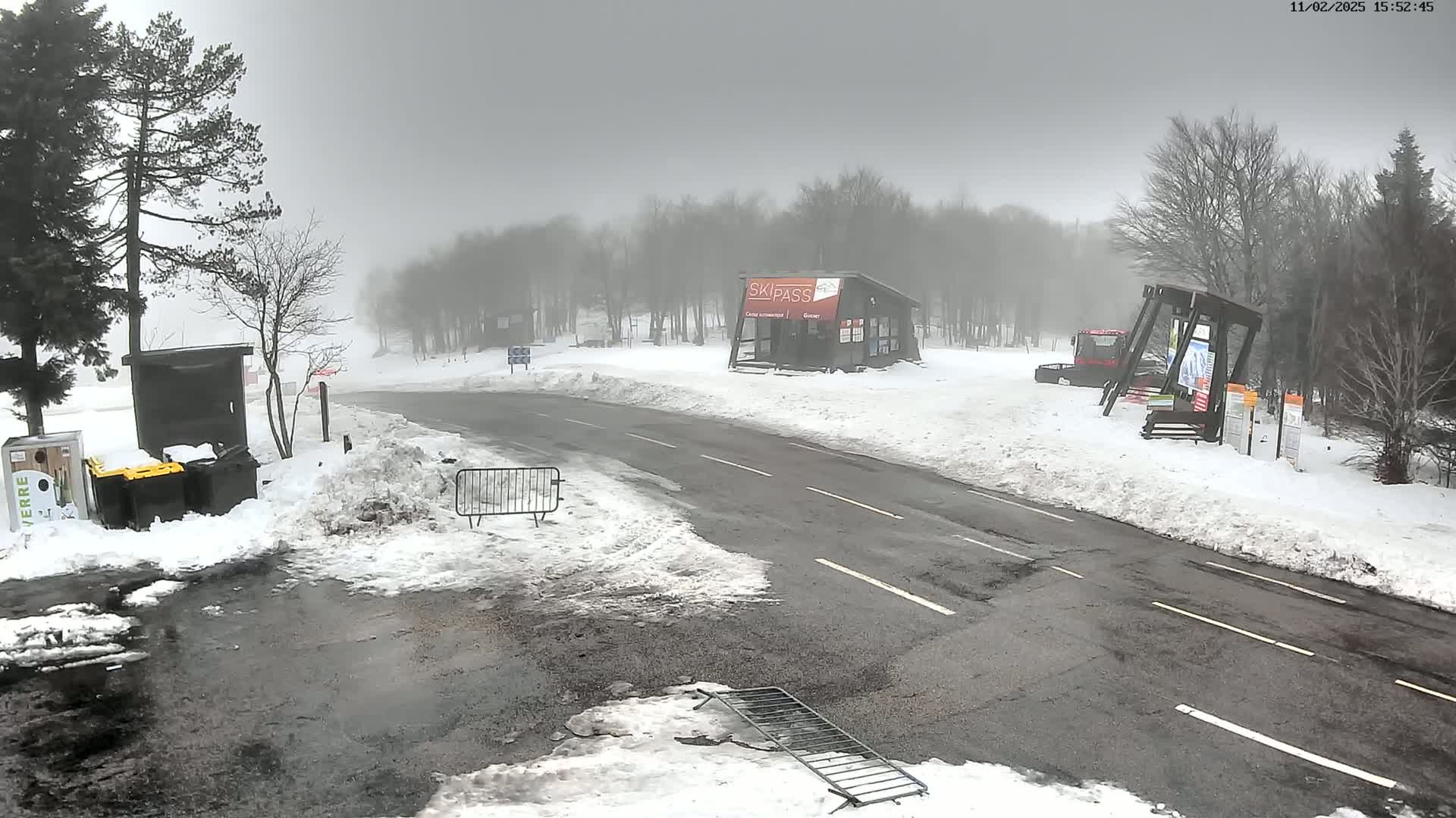 A snow-covered road leads to a ski pass building in a foggy, snowy landscape.