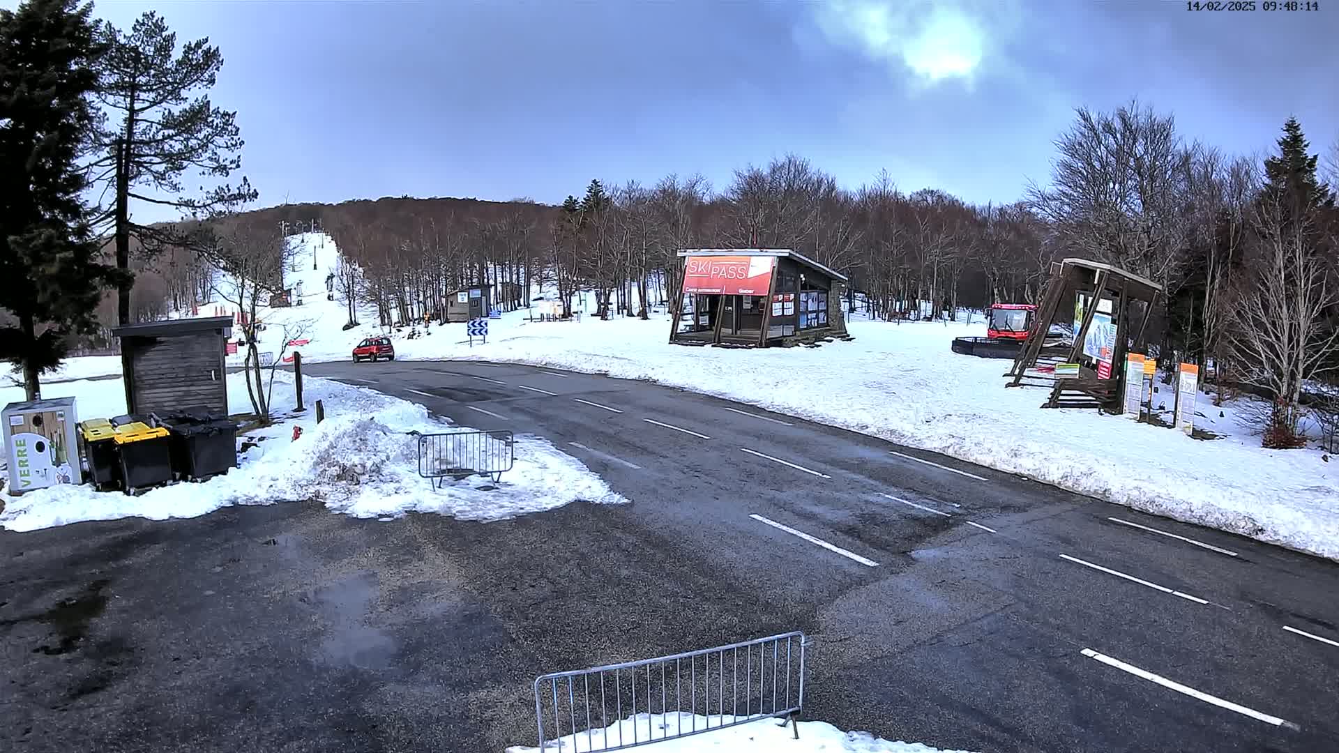A paved road leads to a ski area with snow-covered ground and buildings, under a mostly cloudy sky.