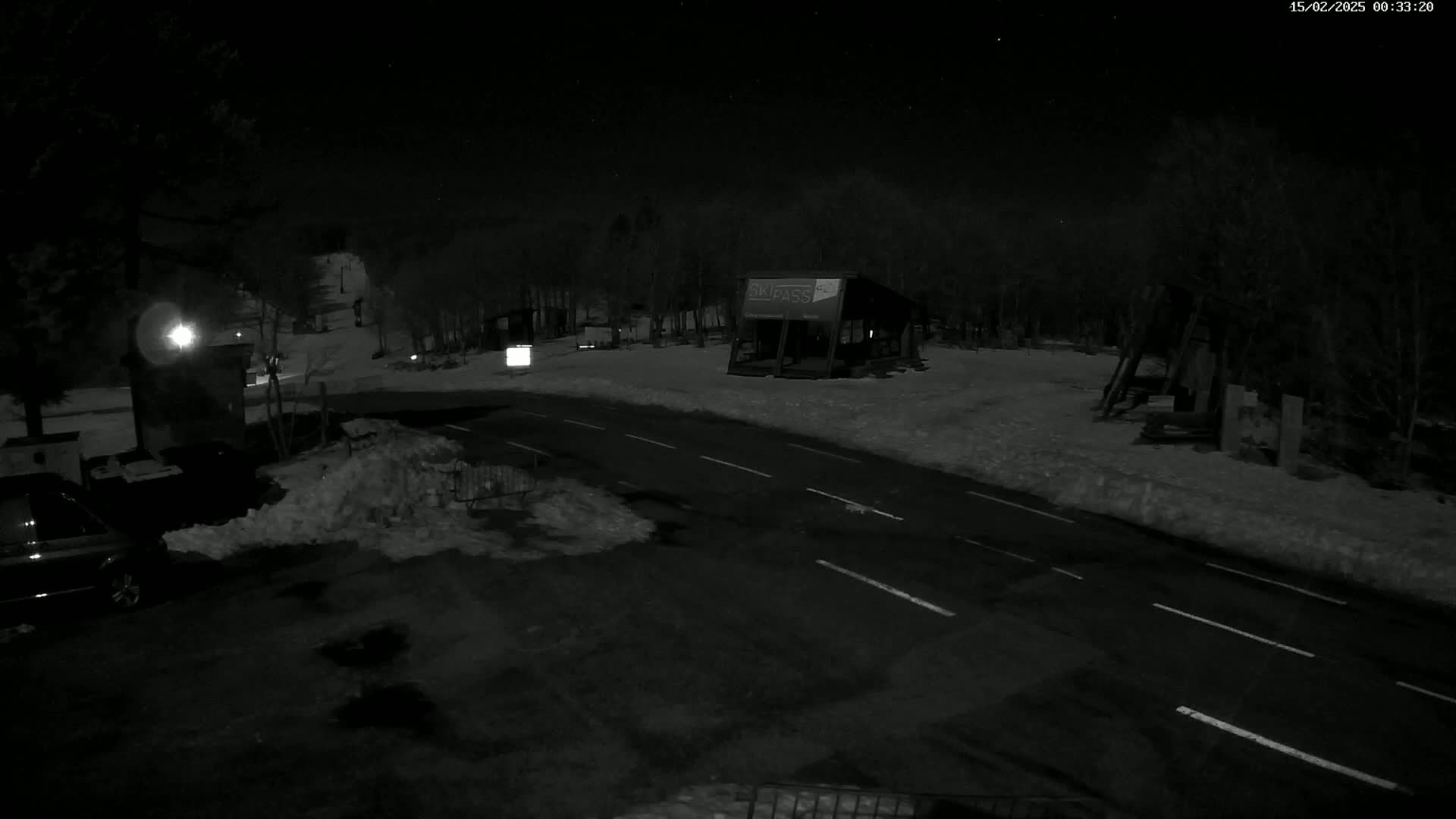 A nighttime, snow-covered road scene shows a small structure, a vehicle, and trees under a starry sky.