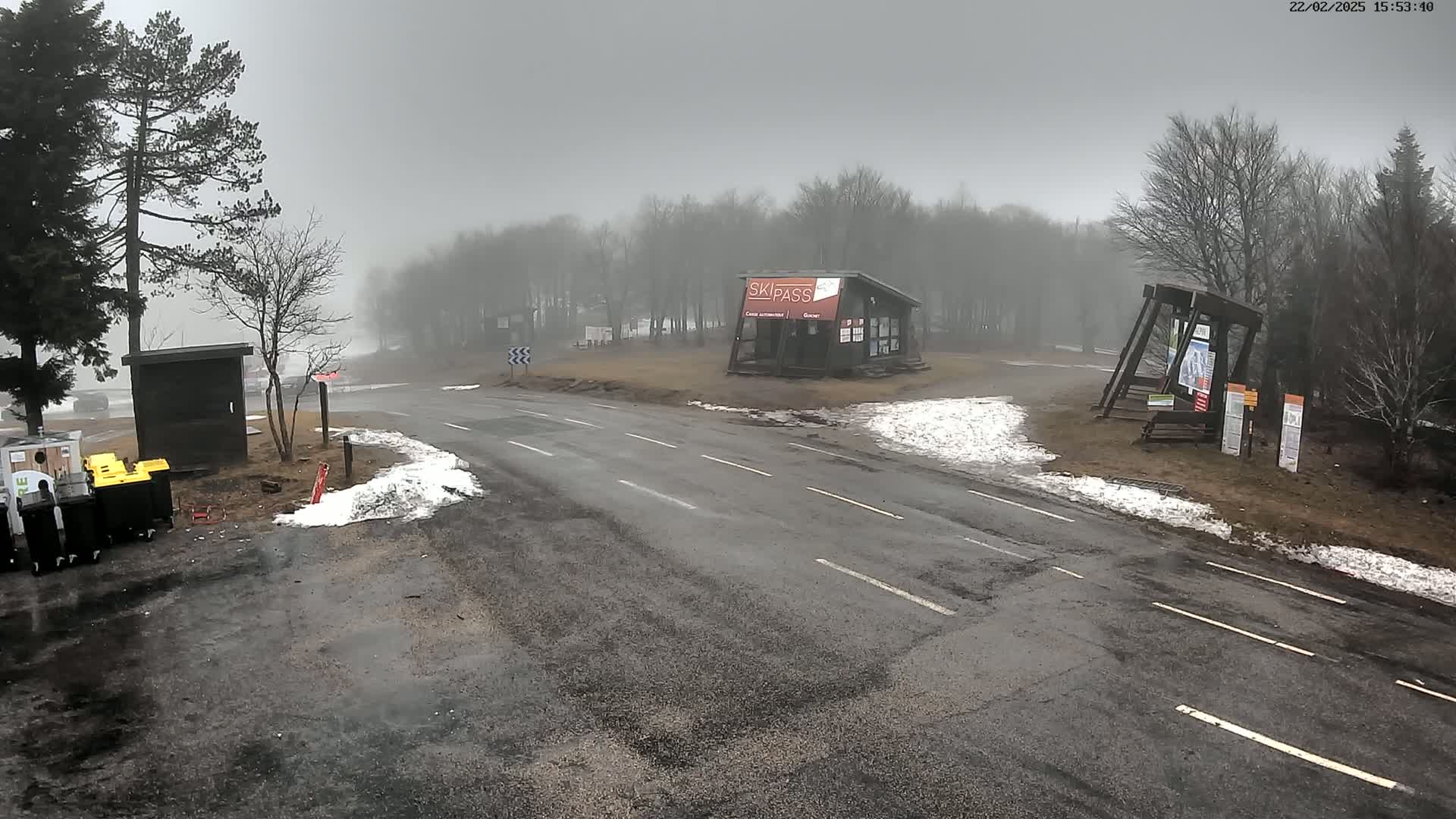 A foggy road intersects near a small building and several trees with patches of snow on the ground.