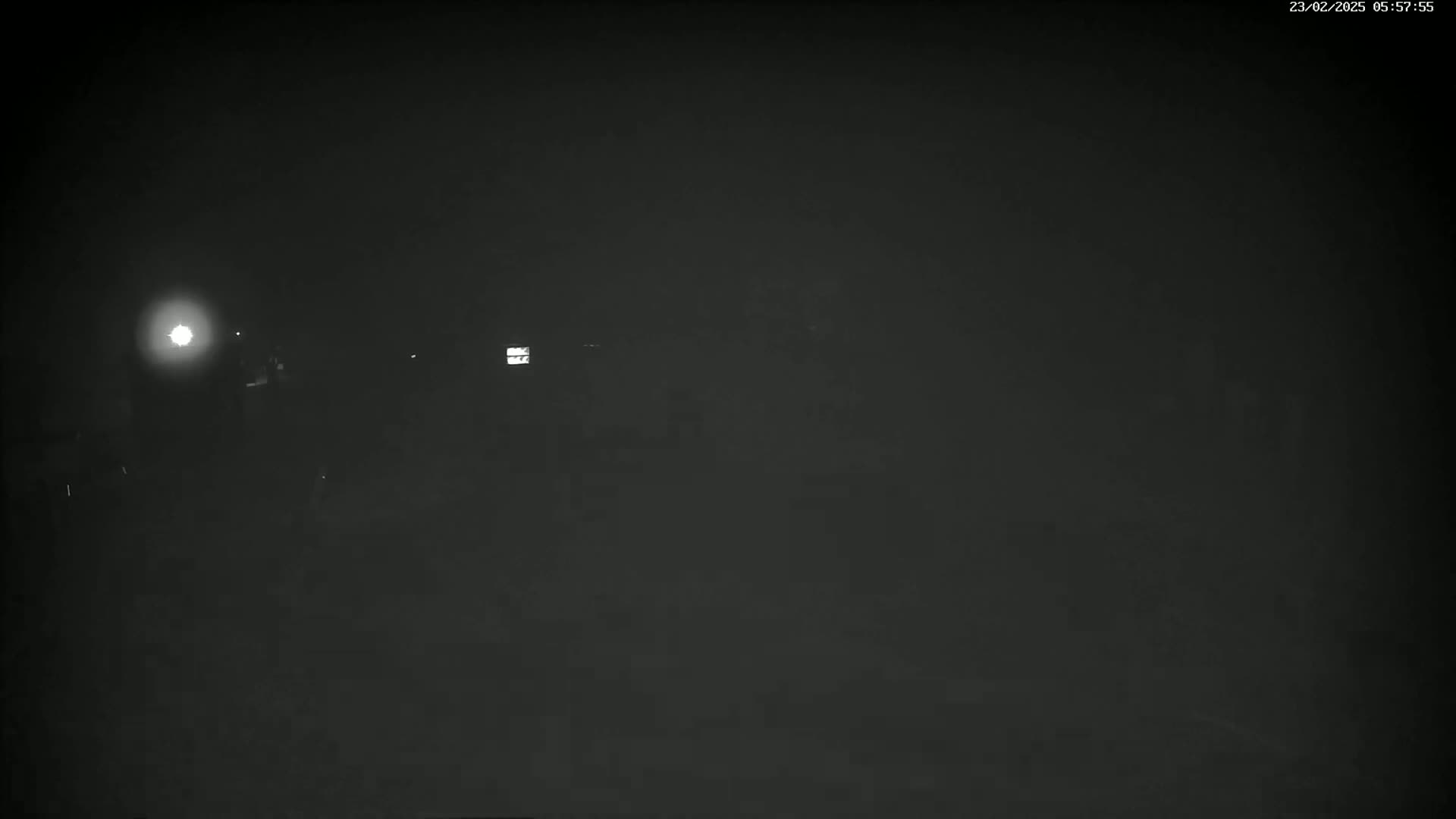 A dimly lit, nighttime scene shows indistinct shapes and a bright light source in the distance.