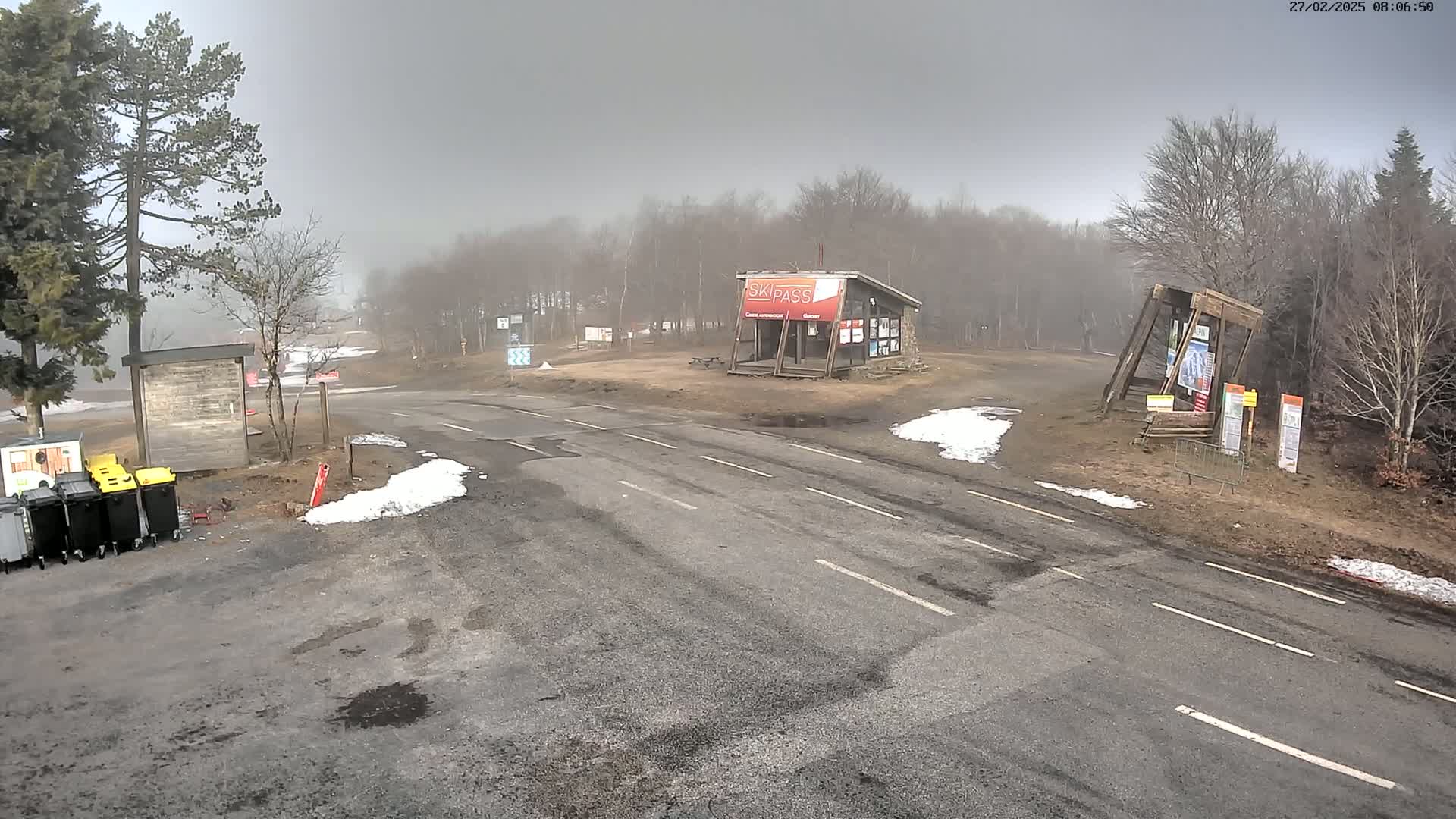 A foggy, overcast day at a ski resort with a paved road and small patches of snow.
