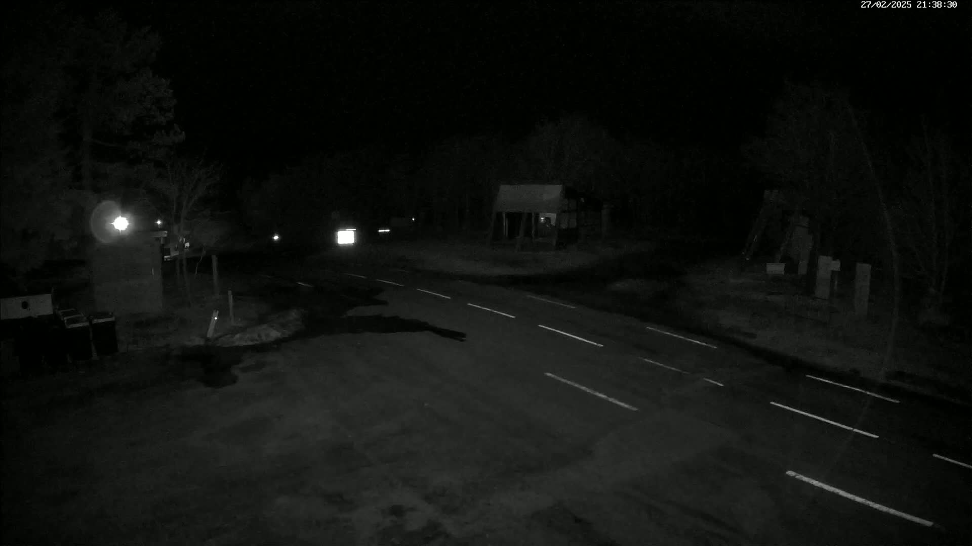 A nighttime, low-light view of a sparsely traveled road with some trees and buildings in the background.