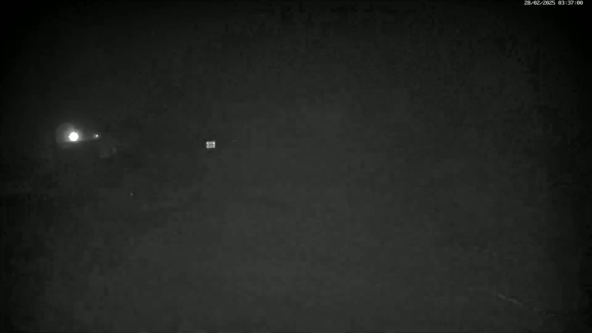 A nighttime, dark scene shows a bright light in the distance under a dark sky.