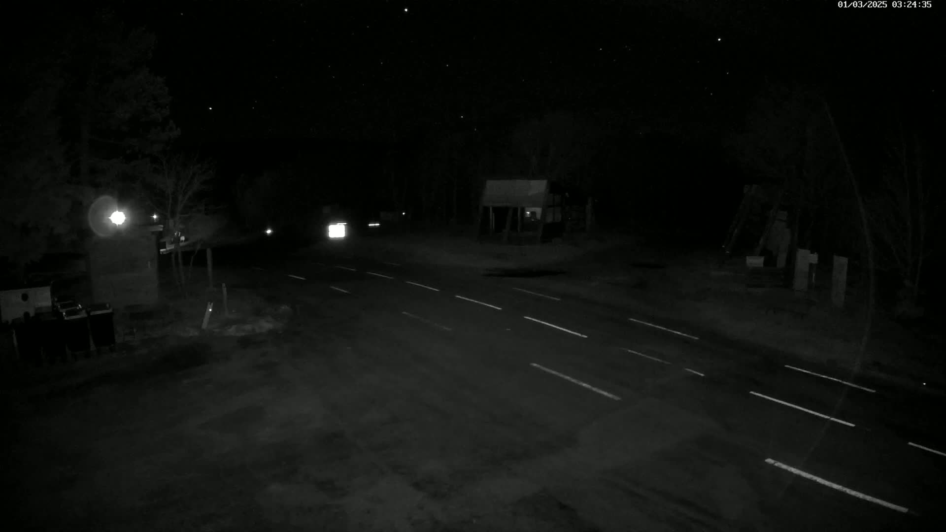 A nighttime view of a sparsely-lit roadway with a few vehicles and some structures visible in the surrounding darkness.