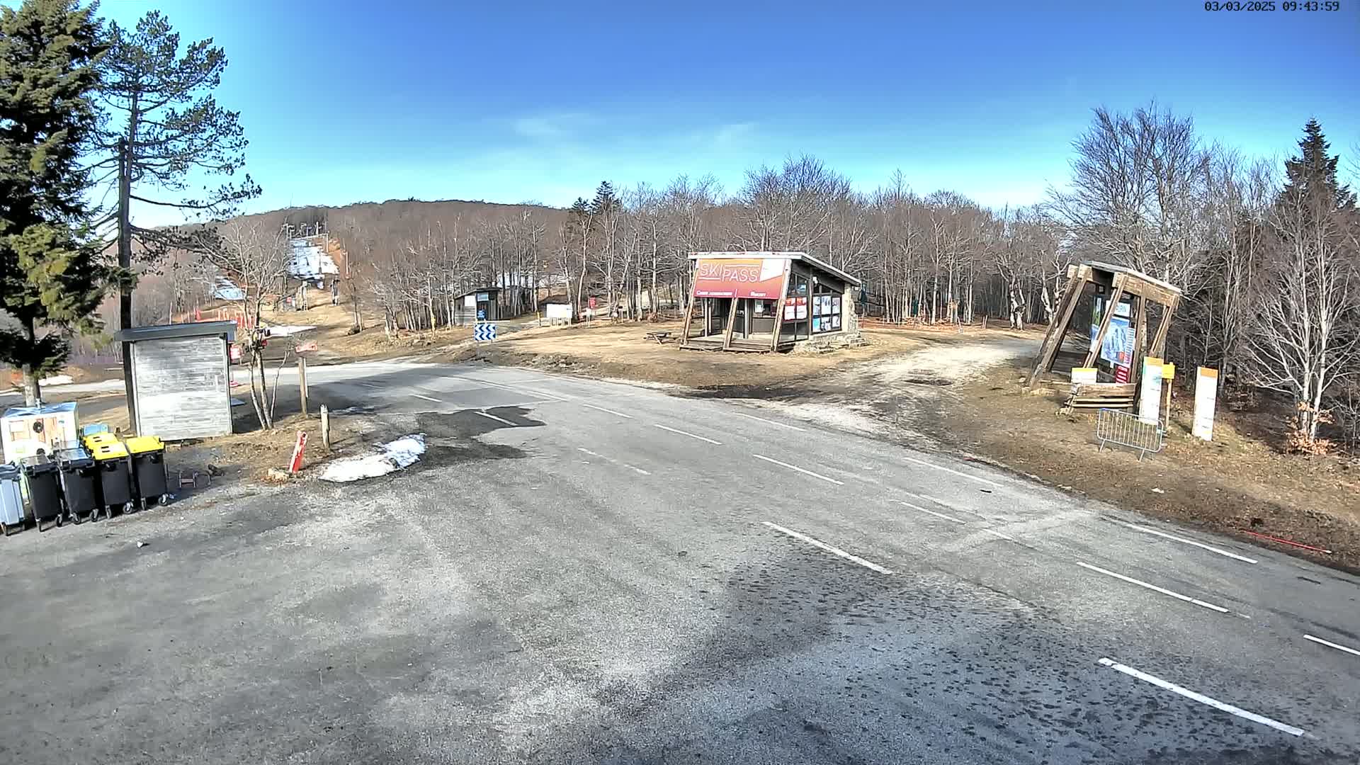 A paved road leads to a ski resort area on a sunny day with patches of snow remaining on the ground.