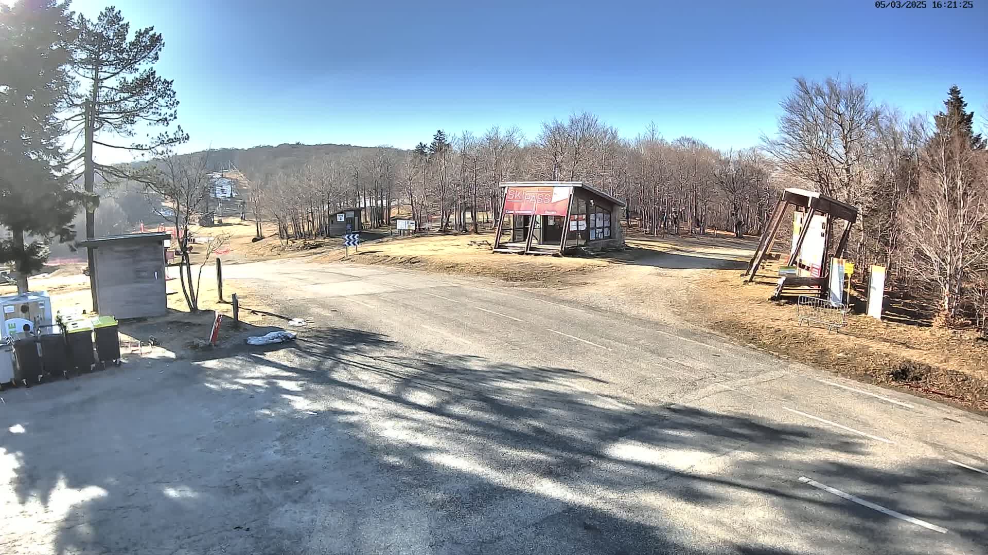 A paved road leads to a ski resort area with small buildings and bare trees under a sunny sky.