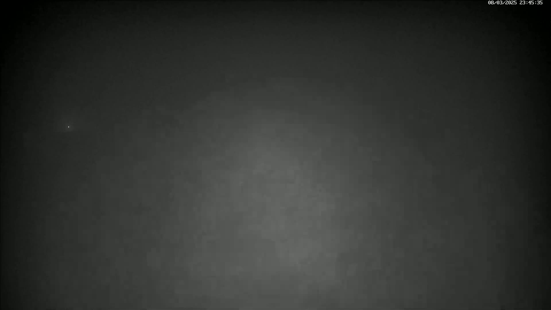 A dark, possibly nighttime, outdoor scene shows a faint, distant light in a hazy or cloudy sky.