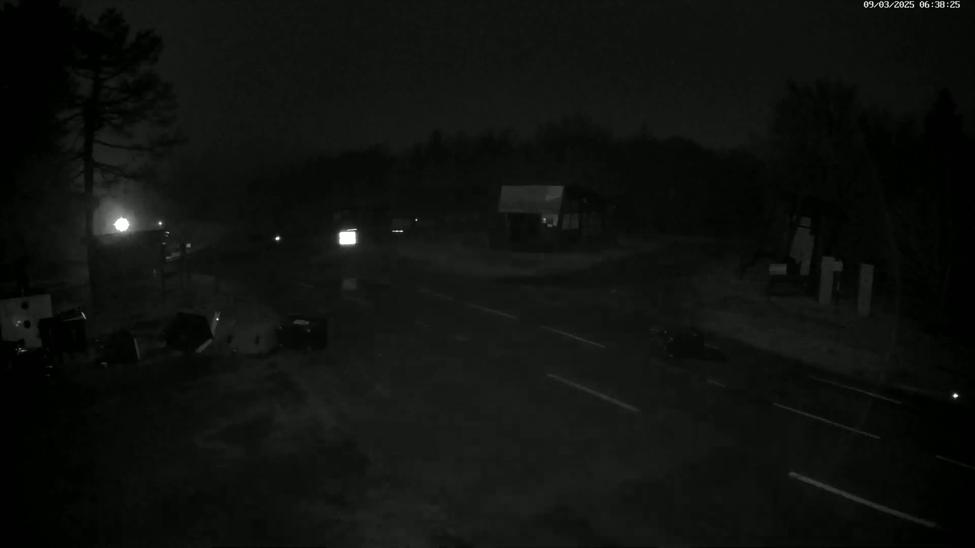 A dark, nighttime scene shows a mostly empty road with a few vehicles and some objects on the side, under a dark sky.