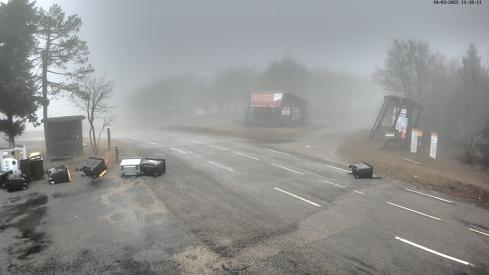 A foggy scene shows a road intersection with several overturned trash receptacles scattered near a small building and trees.