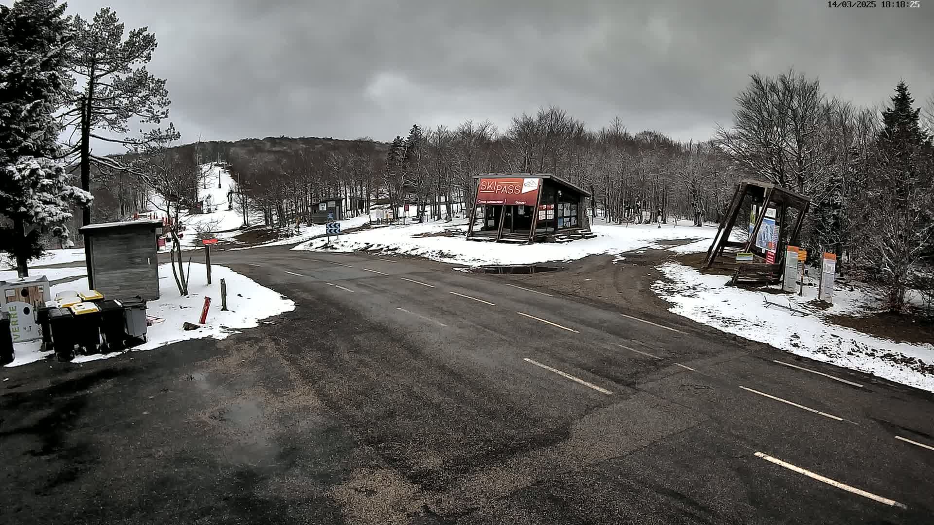 A snow-covered ski resort parking lot with a road leading to a ski lift, under an overcast sky.