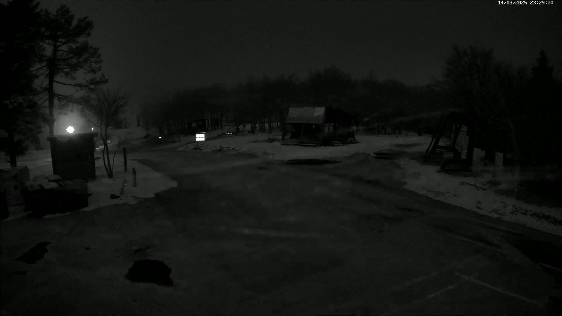 A snow-covered parking lot and small building are visible at night under a dark sky.