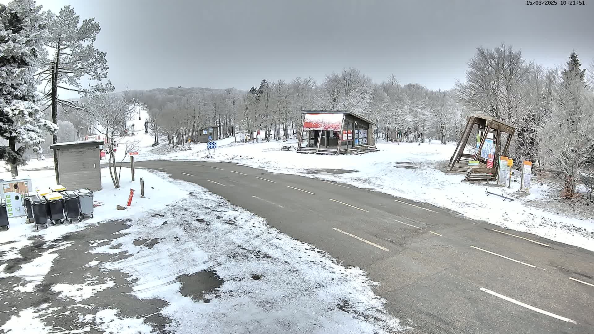 A snow-covered road winds through a wintery landscape, passing small buildings and a ski slope.