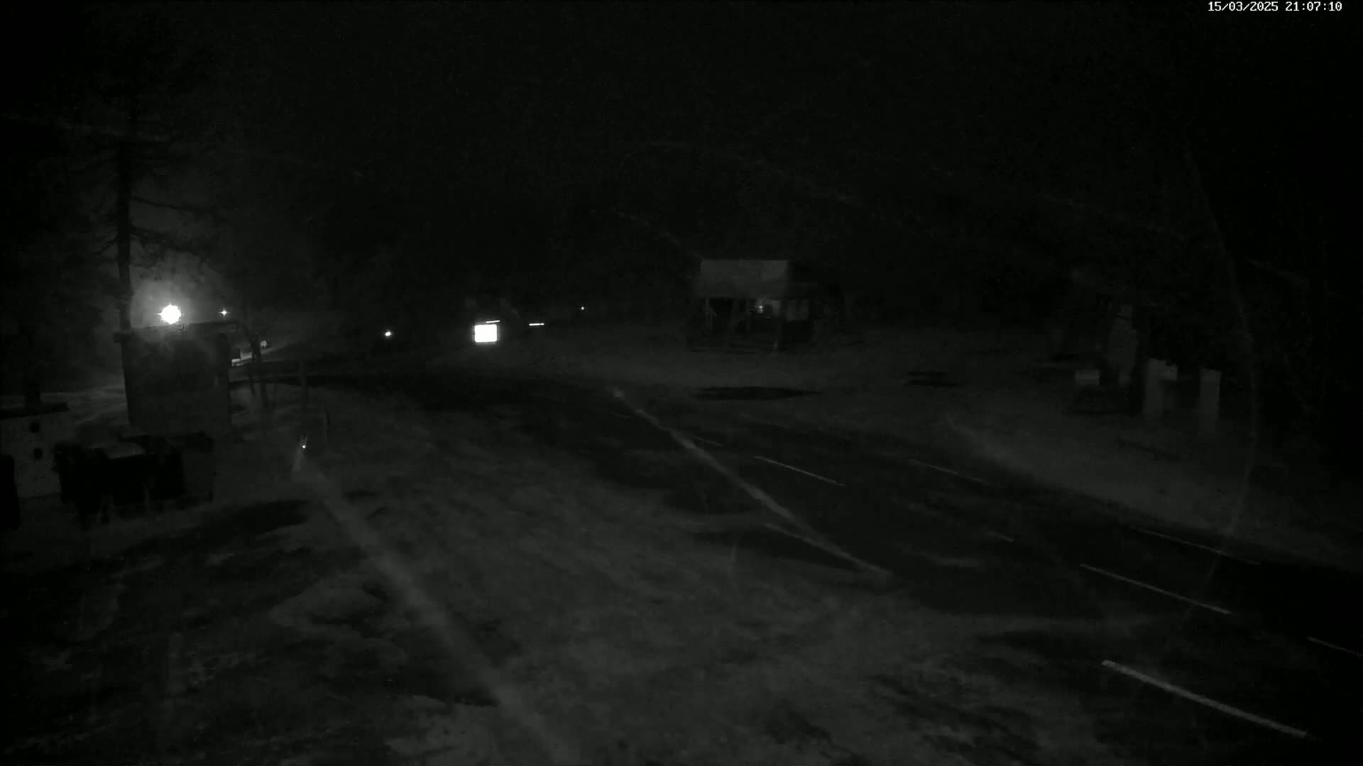 A dark, snow-covered road at night with a few vehicles visible in the distance under heavy snowfall.