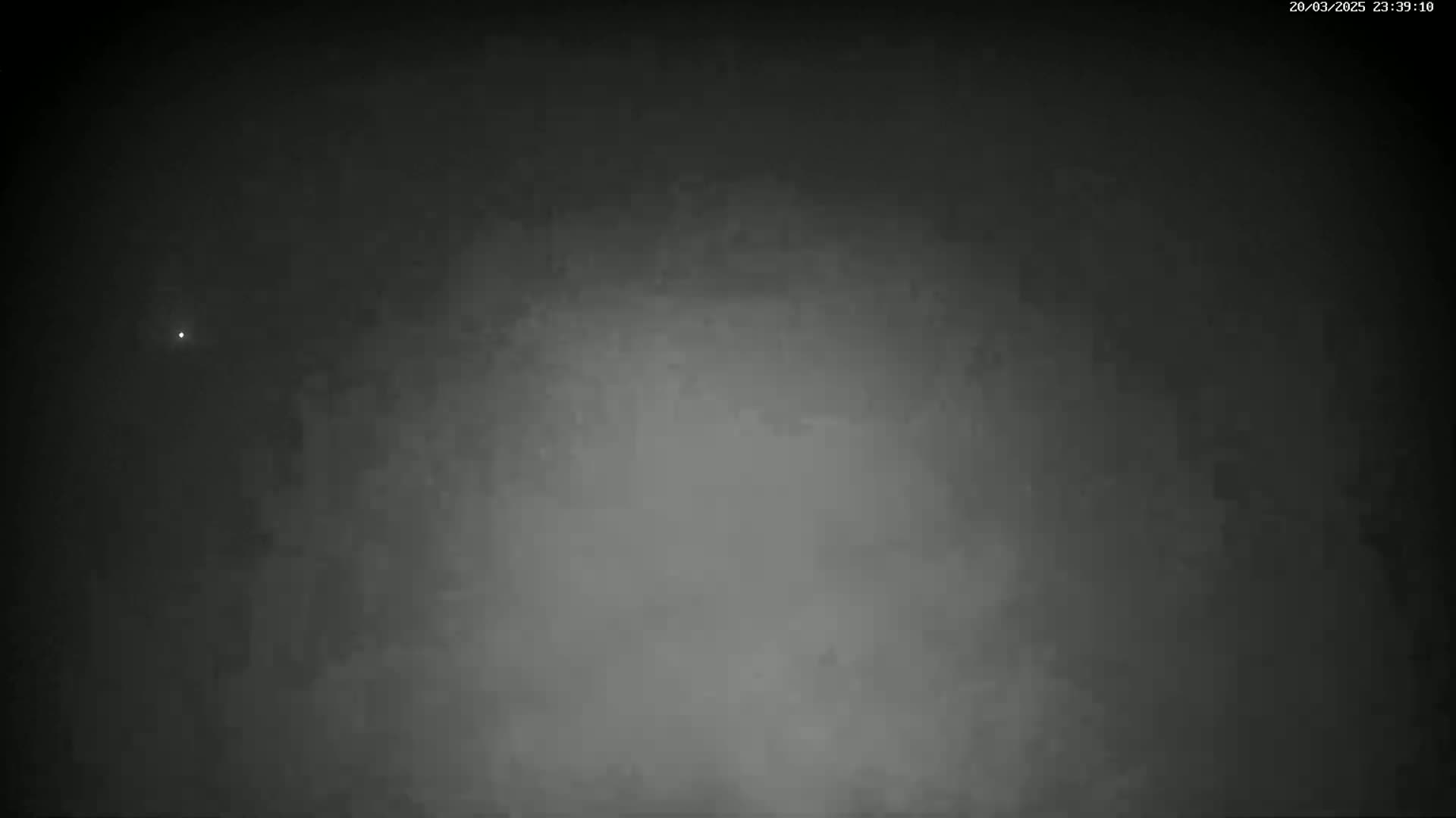 A nighttime image shows a dark, hazy sky with a single, faint light visible.