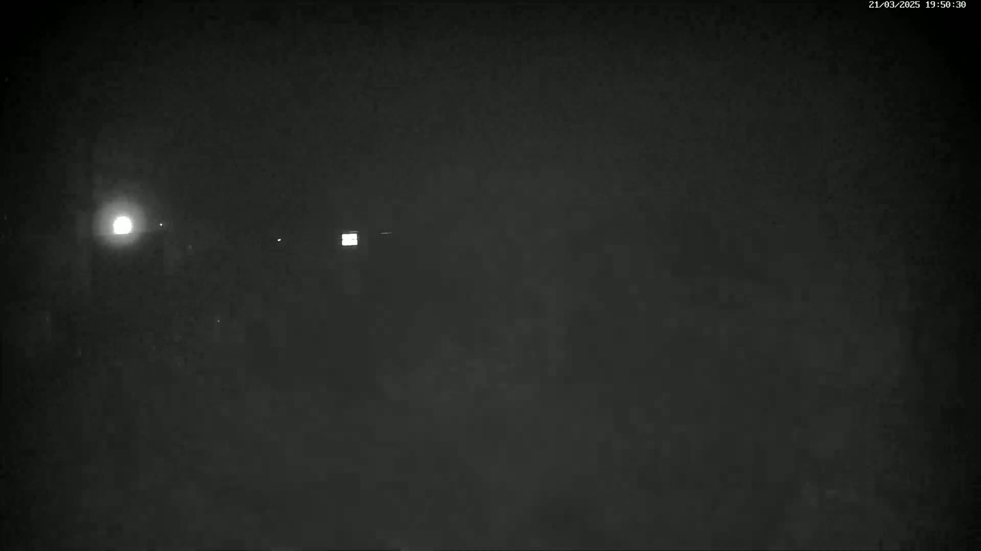 A nighttime, dark scene shows faintly lit areas and a few distant lights in foggy or hazy conditions.