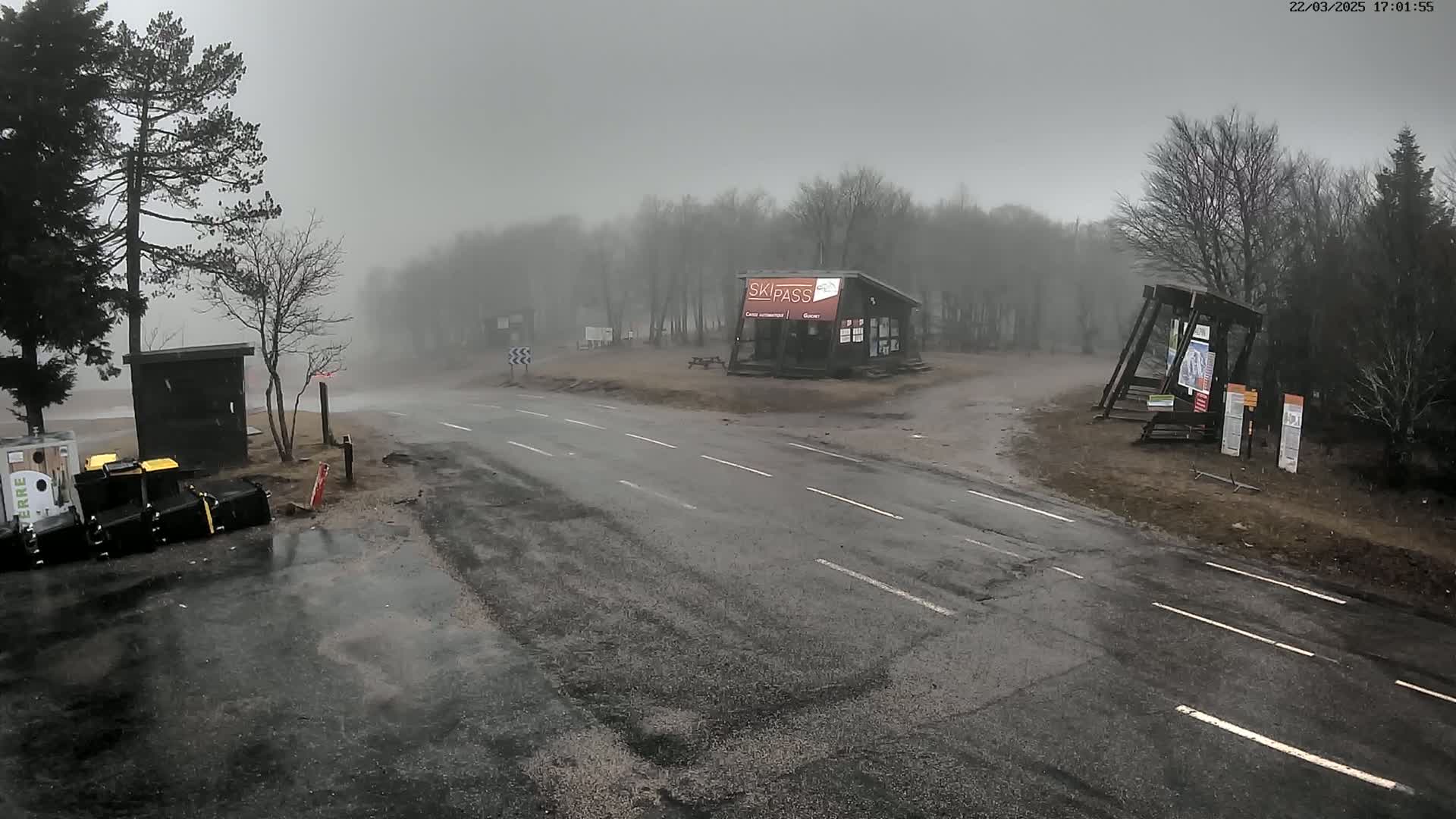 A wet road intersects in front of a small building in a foggy, wooded area.