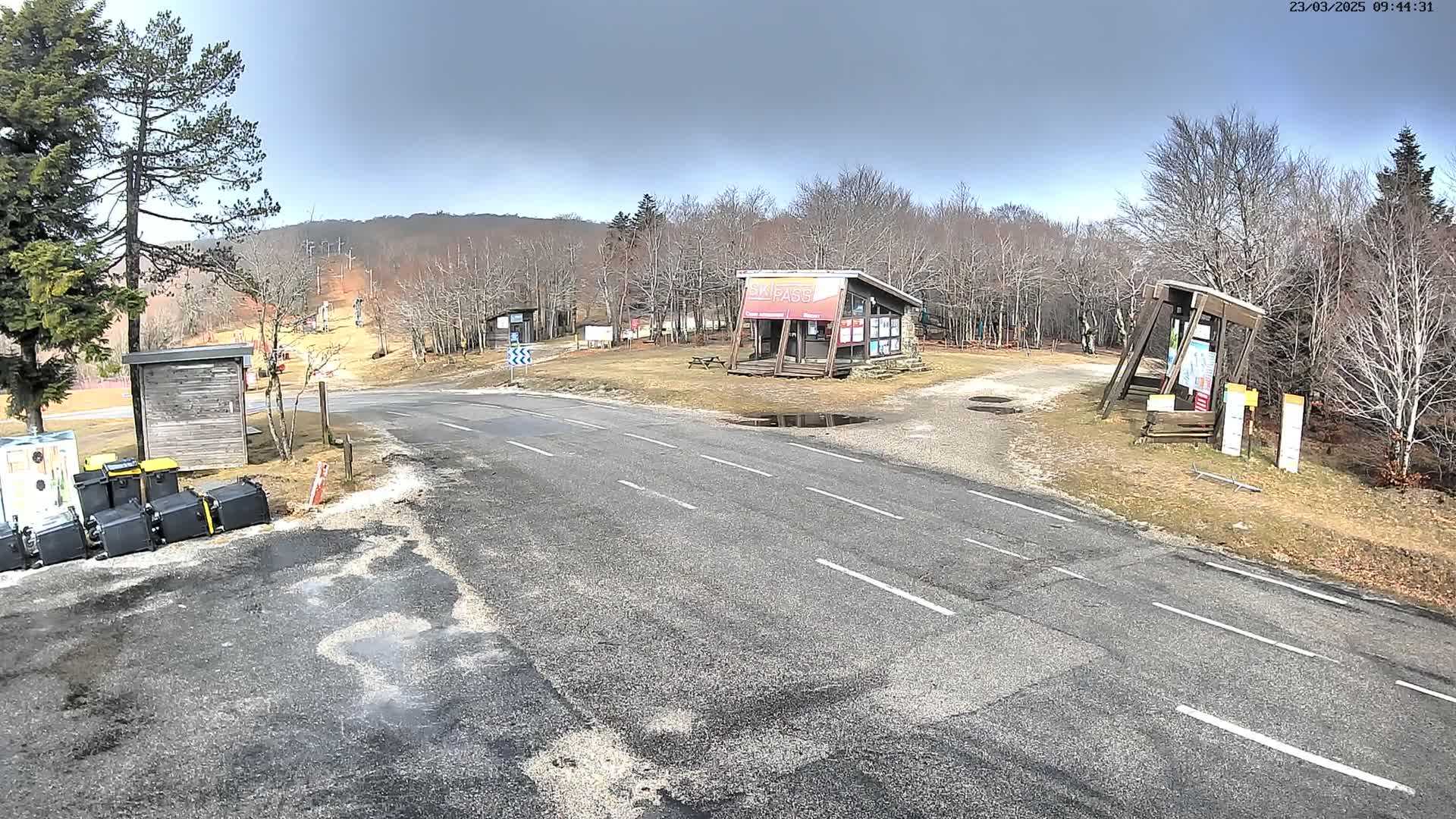 A paved road leads to a ski resort area with several small buildings, under a partly cloudy sky.