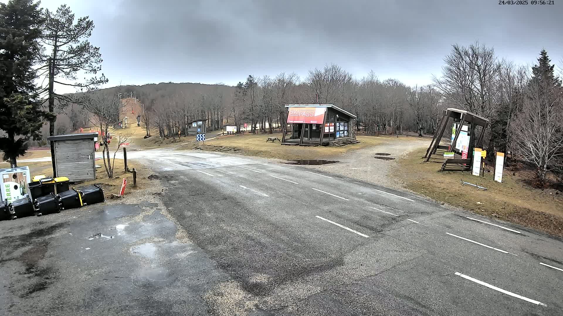 A paved road leads to a ski lift and several small buildings in a wooded area under an overcast sky.