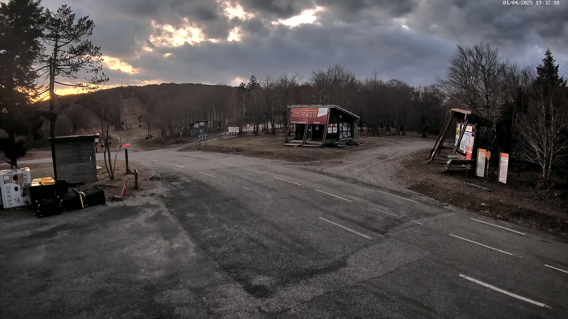 A paved road intersects with a dirt road at a ski resort under a partly cloudy sunset sky.