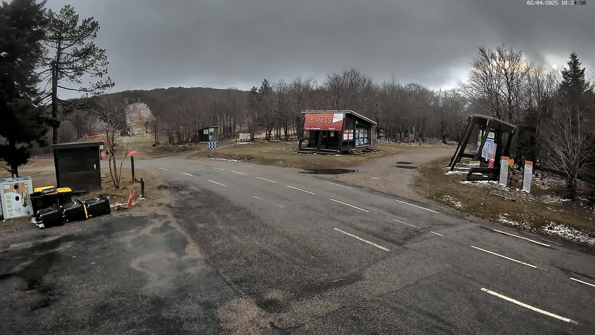 A paved road leads to a ski area under an overcast sky, with some snow patches visible on the ground.