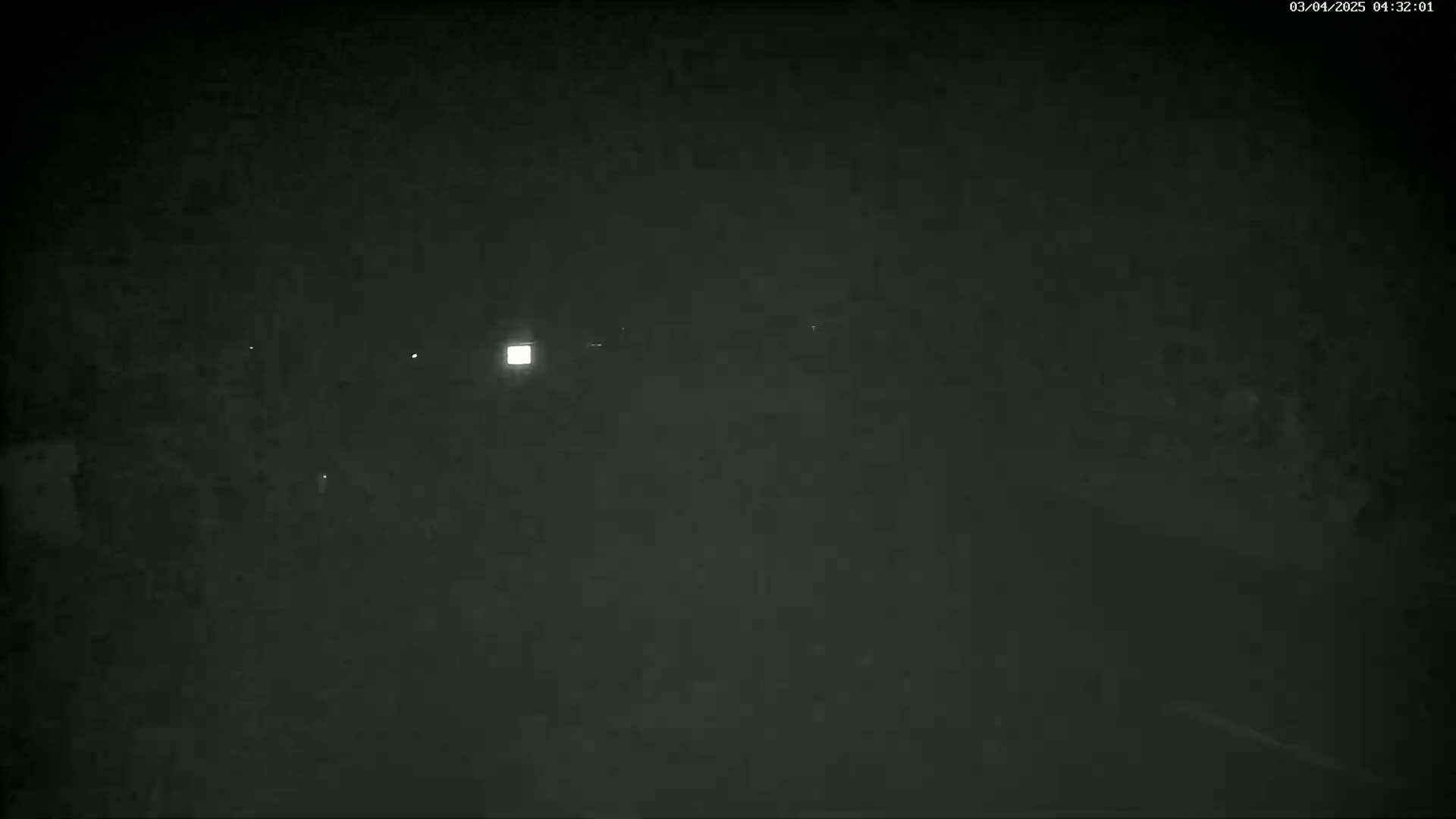 A nighttime, dark, grainy image shows a few faint lights in the distance.