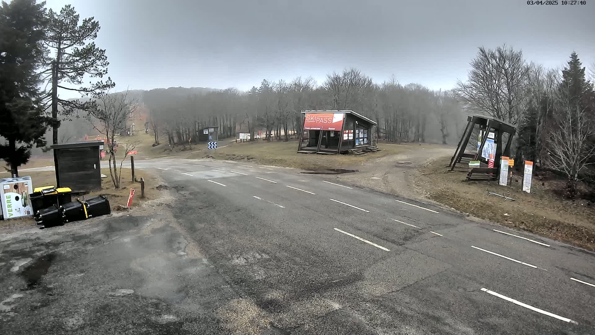 A paved road leads to a ski area under an overcast sky, with a small building and various signage visible.