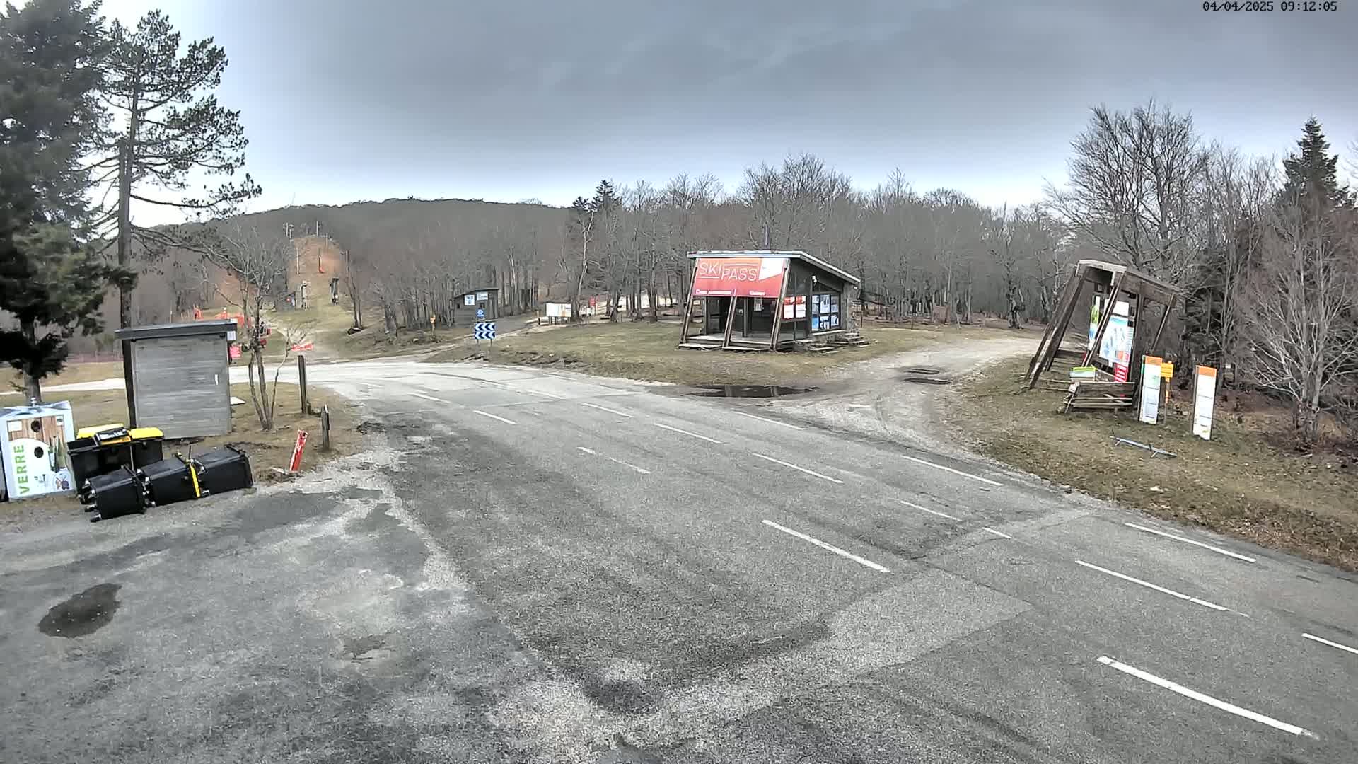 A paved road leads to a ski area with a small building, under an overcast sky.