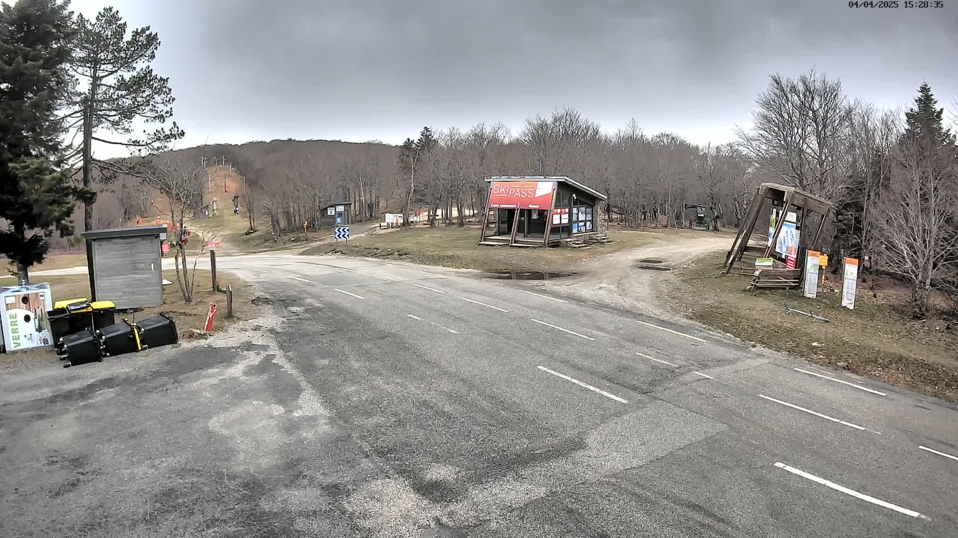 A paved road intersects with a dirt road at a ski area under an overcast sky, with several small buildings and overturned trash cans visible.