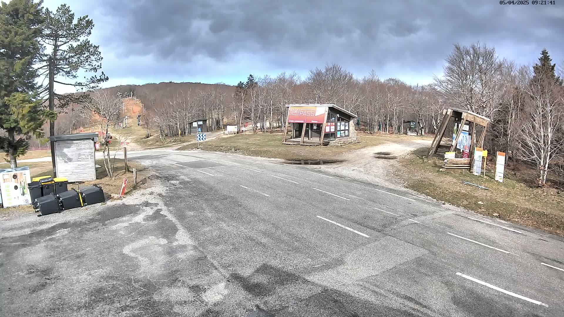 A paved road leads to a ski resort area under a cloudy sky, with bare trees and a few buildings visible.