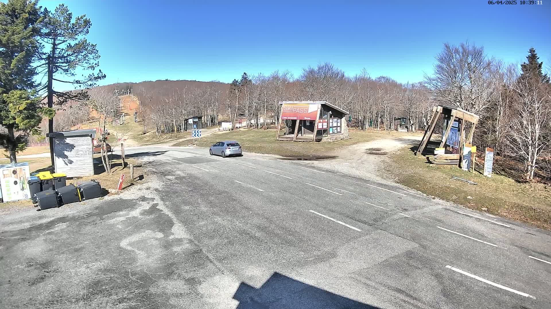 A silver car is parked on a paved road in front of a ski resort on a sunny day.